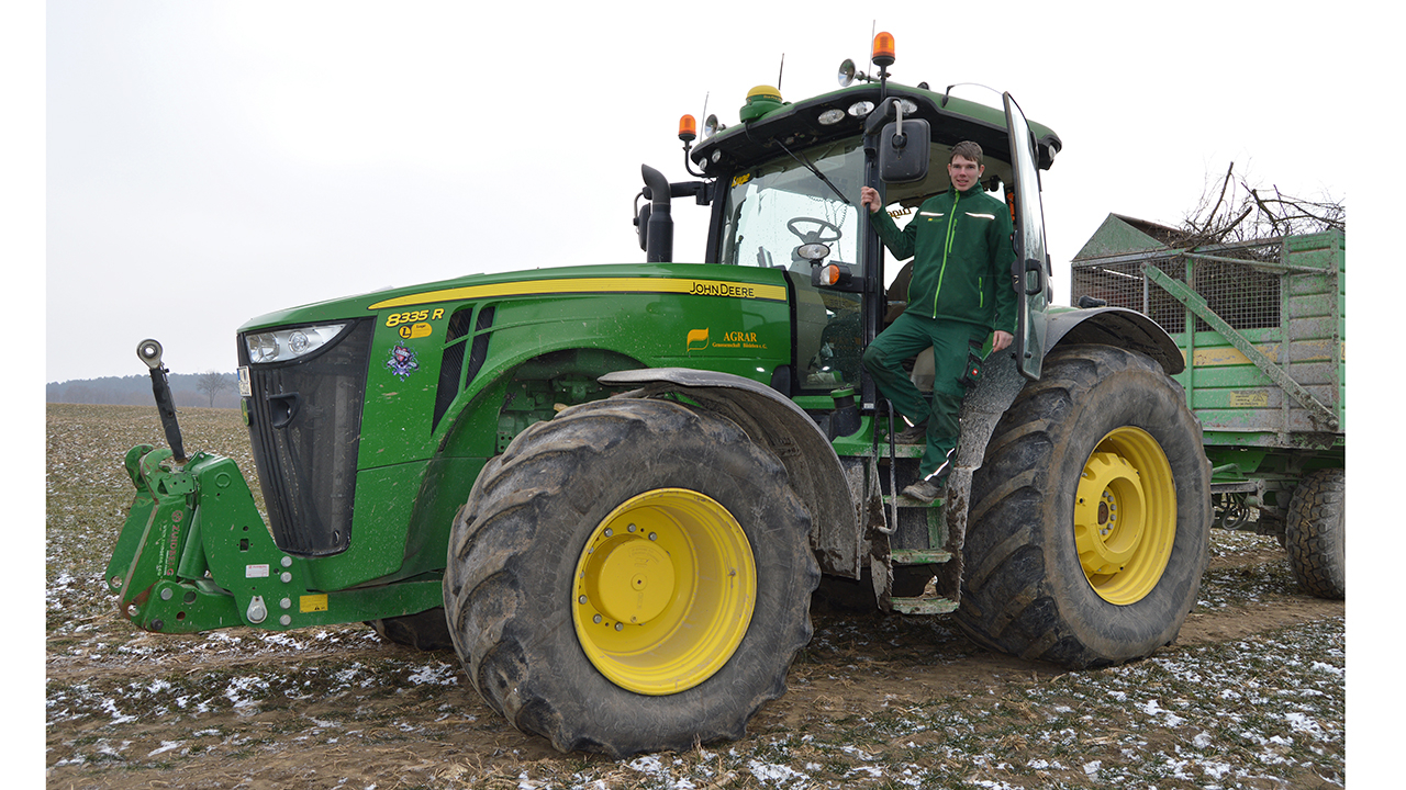 Bild eines John Deere Traktors auf einem Feld. Ein Mitarbeiter schaue aus der Tür raus.