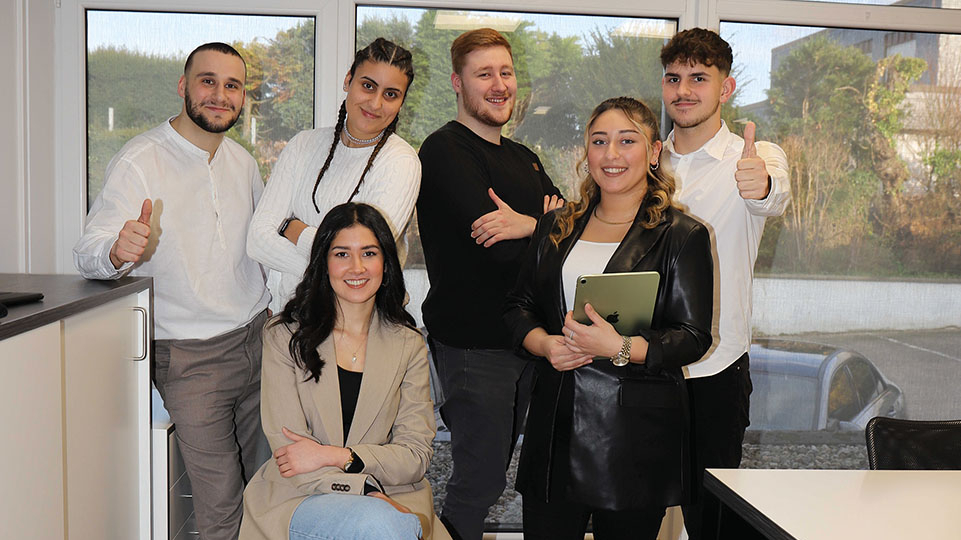 6 Personen stehen im Büro und schauen in die Kamera