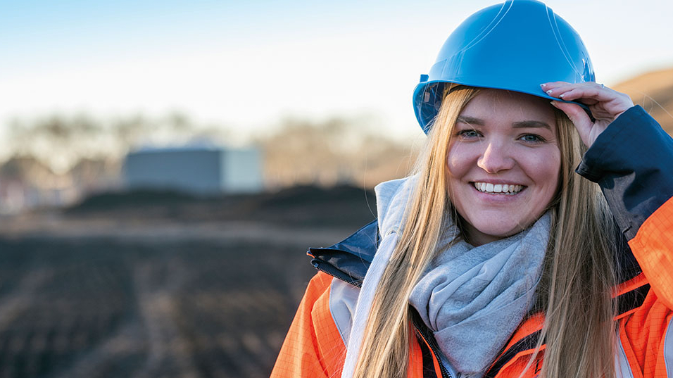 Mädchen in orangener Jacke mit blauen Arbeitshelm