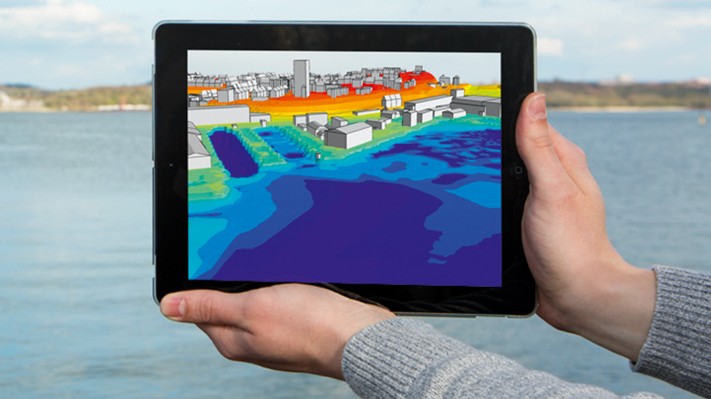 Person hält ein Tablet mit einer Simulation der Küstenbebauung über eine Wasserfläche