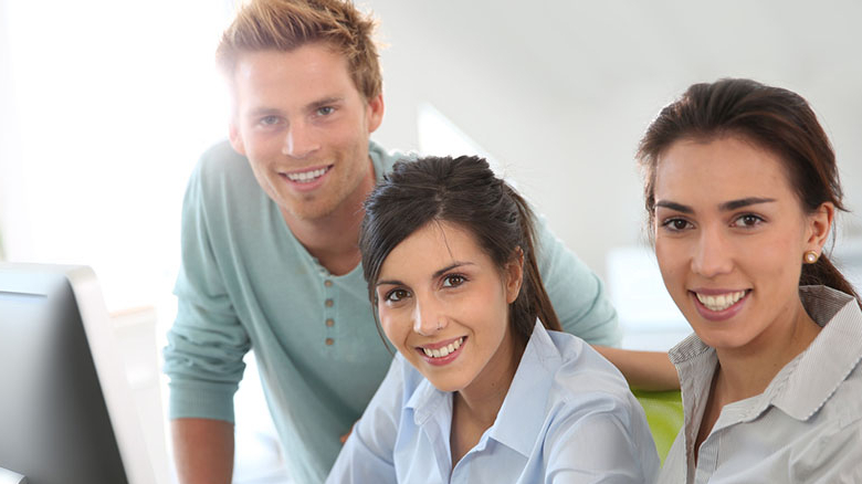 Drei Personen in einem Büro blicken lächelnd in die Kamera