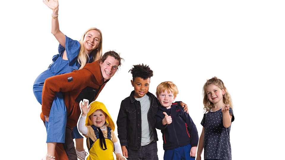 Kinder und Erwachsene lächeln und winken in die Kamera. 