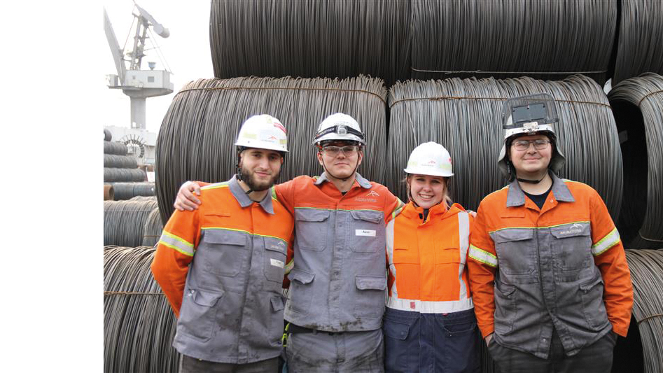 Vier Mitarbeitende in Arbeitskleidung vor großen Drahtrollen