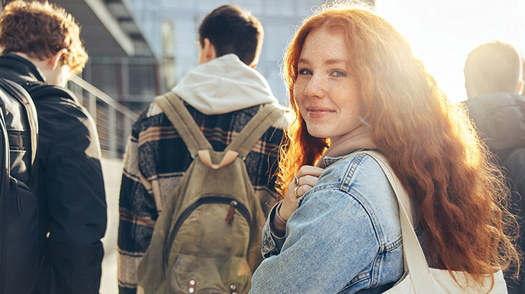 Drei junge Männer, die von hinten zu sehen sind und an einem Gebäude entlanglaufen. Eine junge Frau hinter ihnen dreht sich zur Kamera um.r