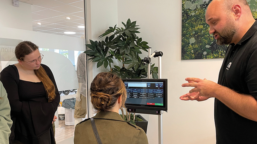 Mann erklärt drei jungen Frauen Funktionen am Monitor