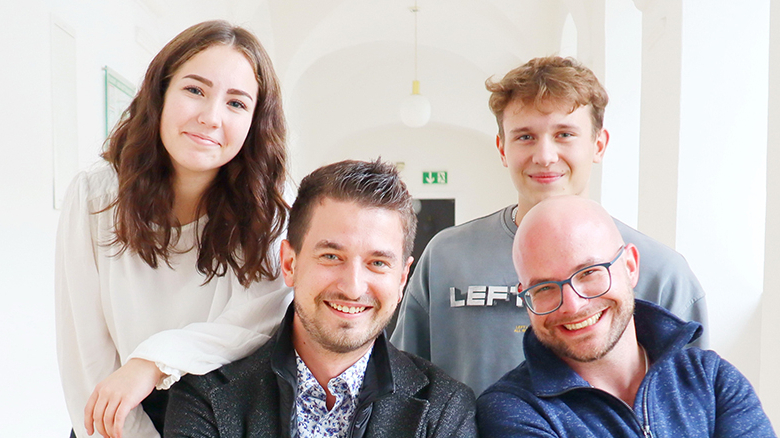 Vier Personen blicken lächelnd in die Kamera