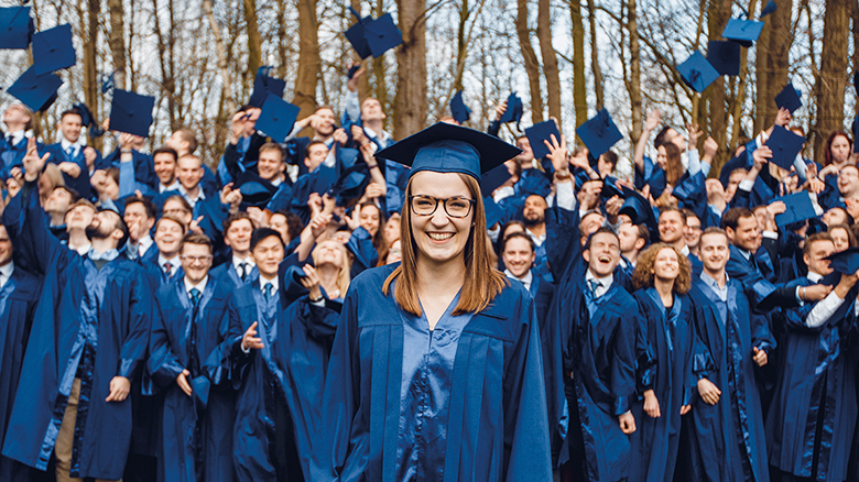Gruppenfoto von Studierenden mit blauen Umhängen, die ihre Hüte in die Luft werfen