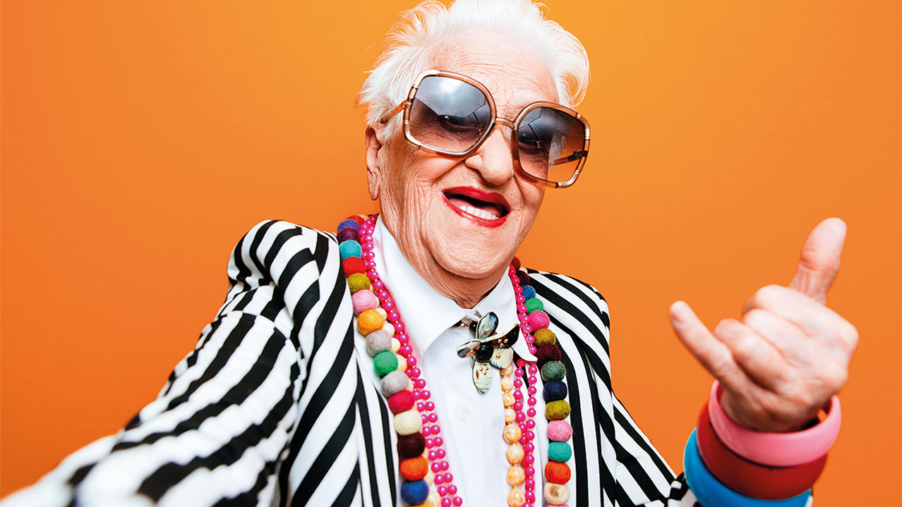 Eine schrill gekleidete ältere Frau mit weißen Haaren und Sonnenbrille