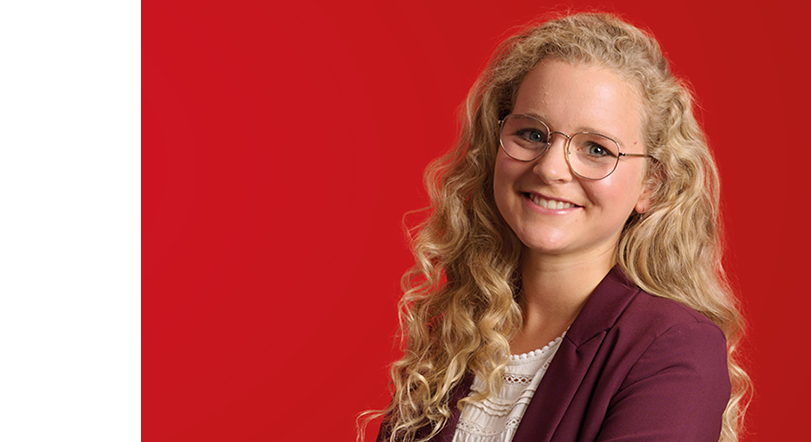 Junge lächelnde Person mit lockigem Haar und Brille vor einem roten Hintergrund