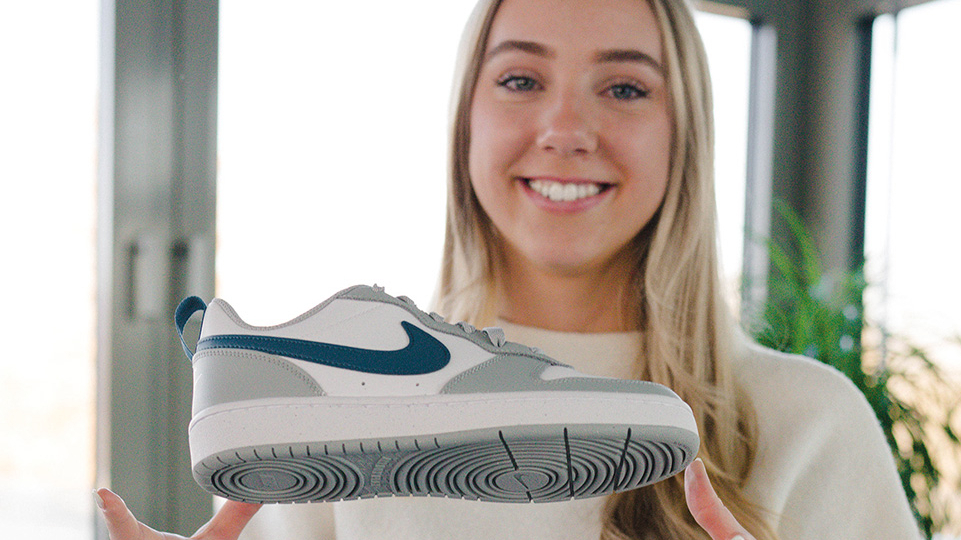 Junge Frau hält lächelnd einen Nike-Schuh in die Kamera