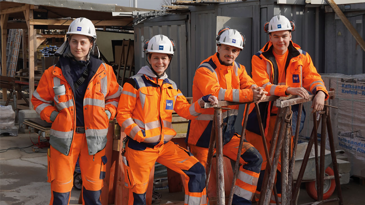 Vier Azubis in oranger Arbeitskleidung