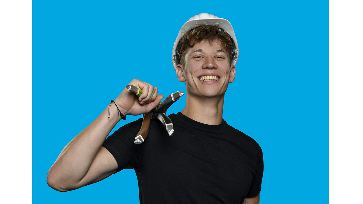 Junger Mann mit Bauhelm lacht in die Kamera. 