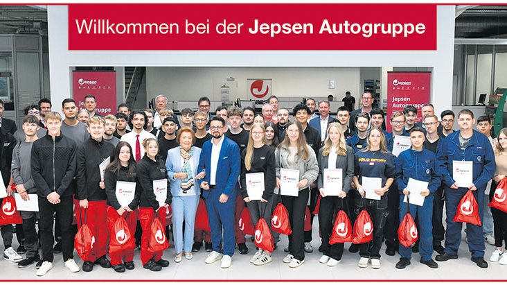 Mitarbeitende der Jepsen Betriebs GmbH & Co. KG stehen vor einem Schild mit der Aufschrift " Willkommen bei der Jepsen Autogruppe" und lächeln in die Kamera.