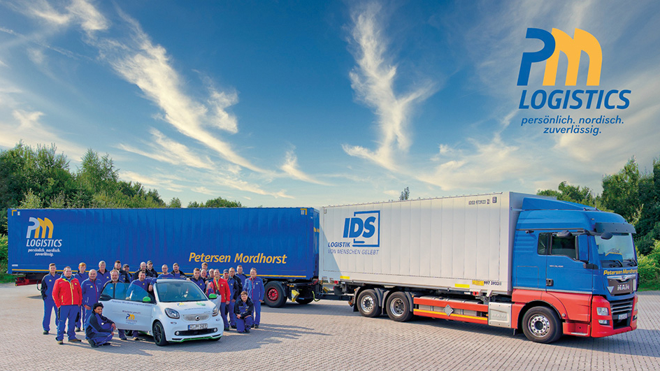 Gruppenfoto der Mitarbeitenden auf einem Parkplatz mit PKW und LKW im Hintergrund