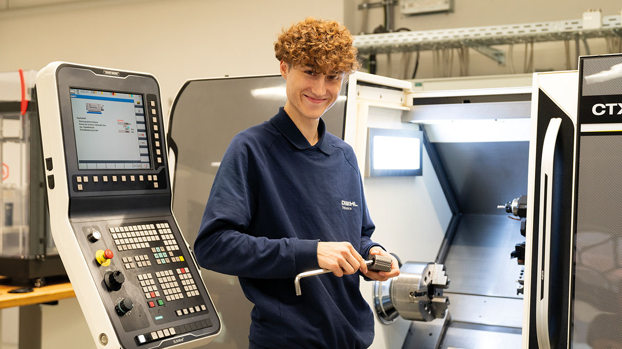 Jugendlicher mit rotem lockigen Haar steht vor zwei Maschinen.