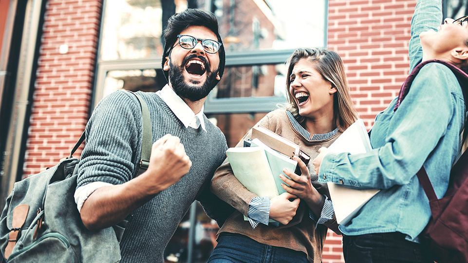 Drei junge Menschen in der Gruppe freuen sich und die linke Person ballt freudig die Faust