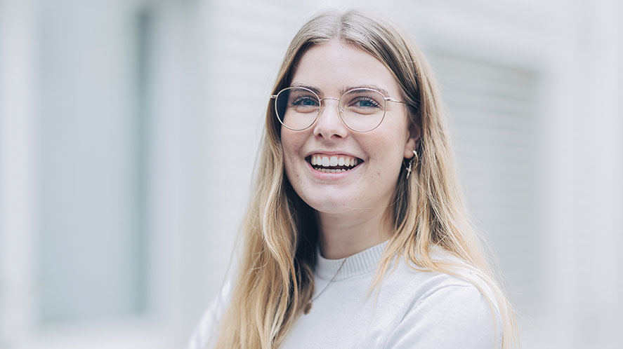 Junge Person mit Brille blickt lachend in die Kamera.