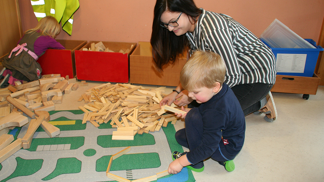 Junge Person und Kind spielen mit Bauklötzern aus Holz