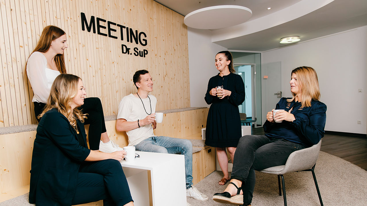 5 junge Menschen zusammen mit einer Tasse in der Hand unterhalten sich.