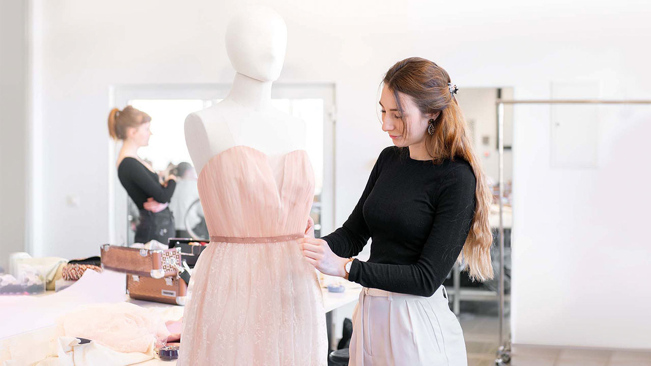 Modedeisgnerin steckt ein rosa Kleid an einer Modepuppe fest.