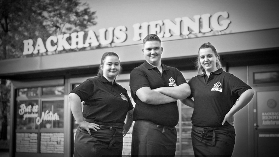 Bild vor Filiale Backhaus Hennig mit drei Mitarbeitenden