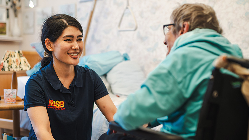 Junge lächelnde Frau von ASB hockt vor einem Rollstuhlfahrer
