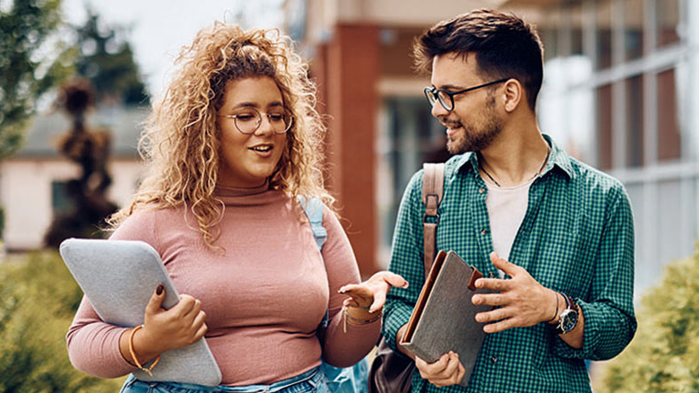 Zwei Personen unterhalten sich. Beide tragen eine Brille und haben einen Laptop in der Hand.