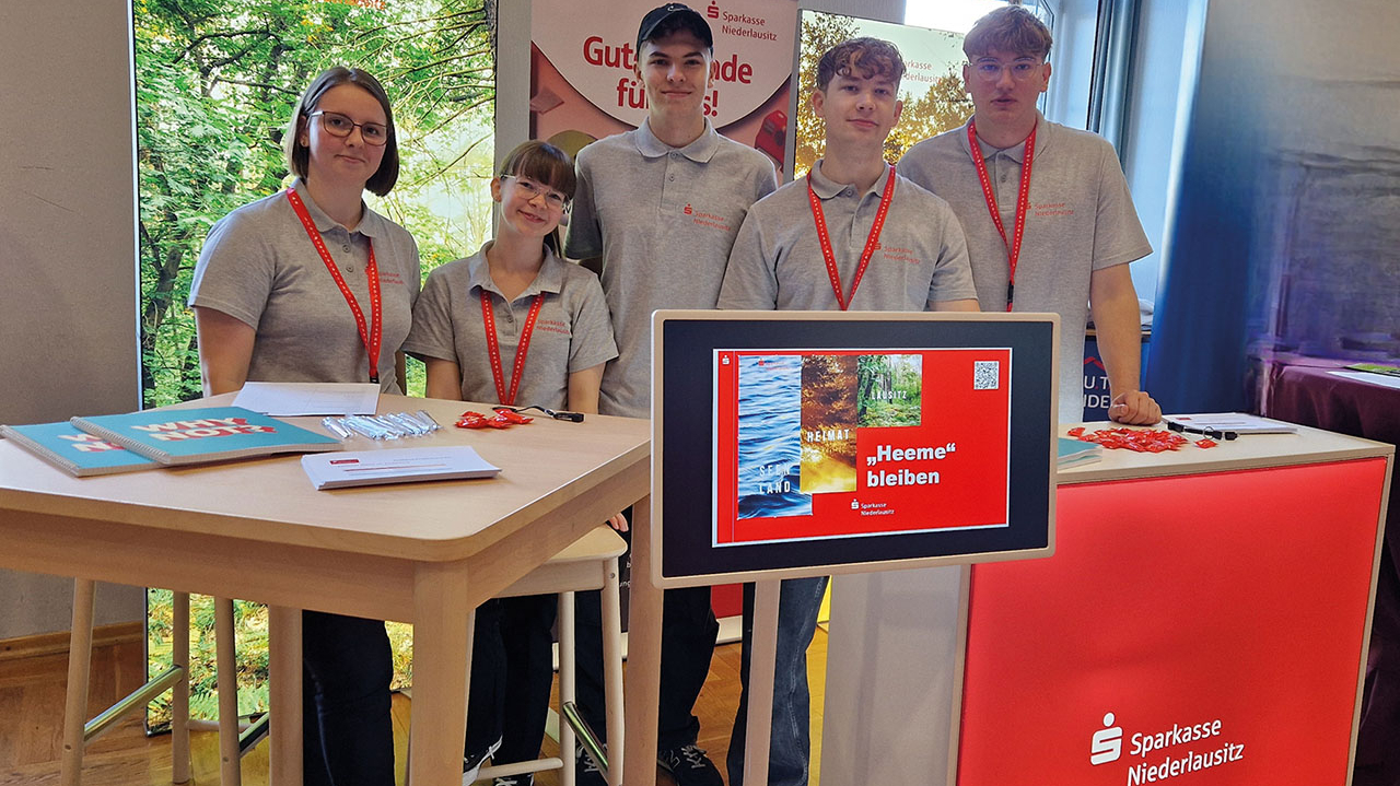 5 Azubis stehen hinter einem roten Messestand der Sparkasse Niederlausitz