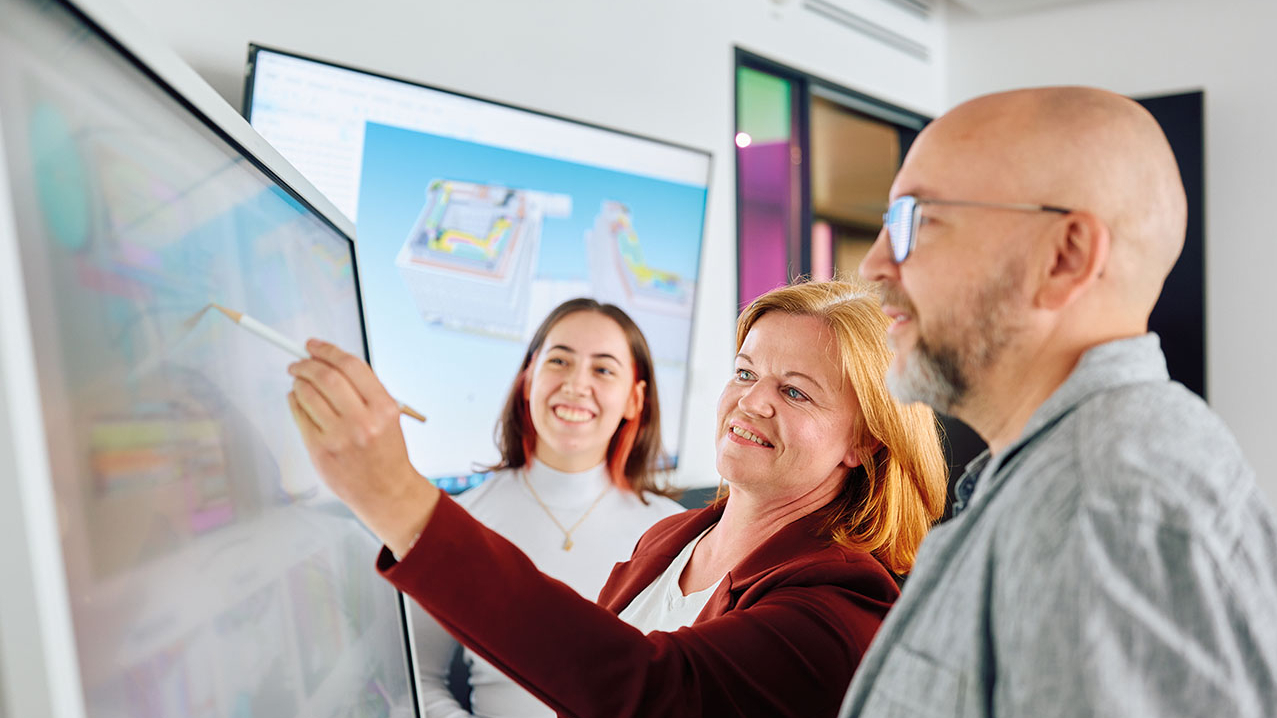 3 Personen stehen vor einer interaktiven Tafel und besprechen sich.