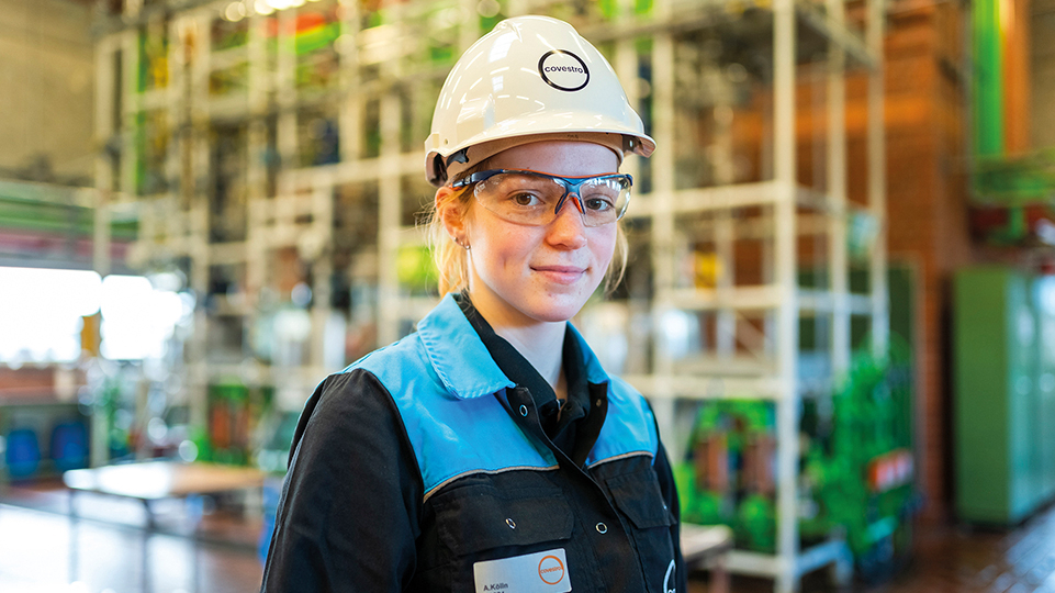 Junge Frau mit Helm und Schutzbrille in Werkshalle