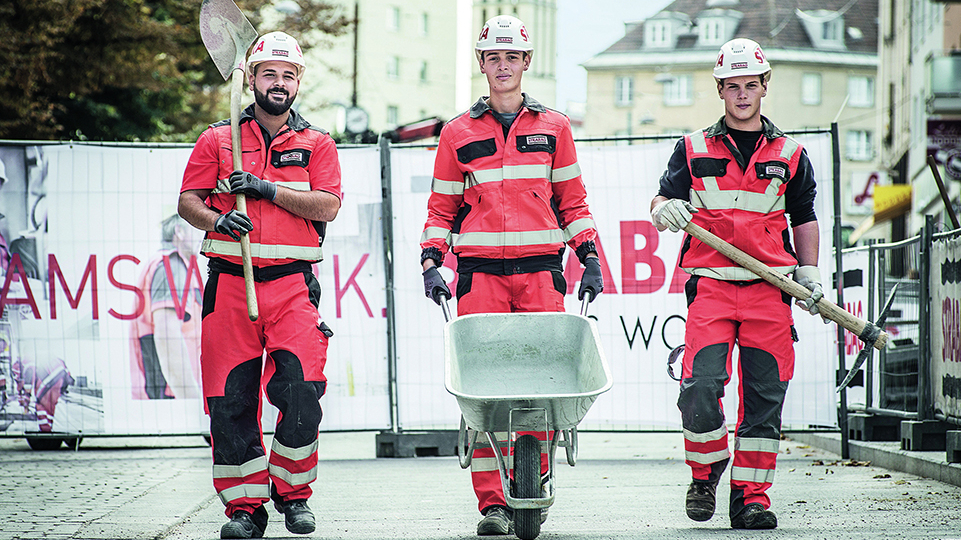 Drei junge Männer in Schutz- und Arbeitskleidung auf einer Baustelle