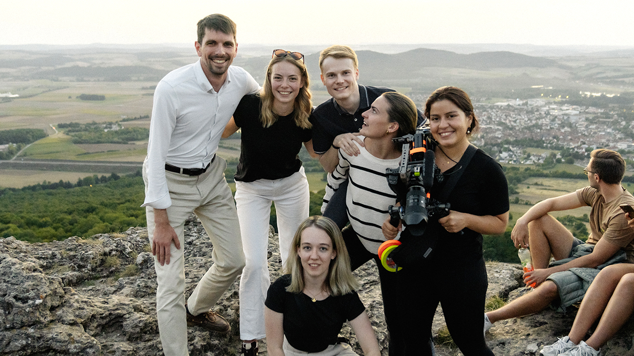 Gruppe junger Menschen stehen auf einem Felsen und machen ein Gruppenbild mit einer ländlichen Landschaft im Hintergrund