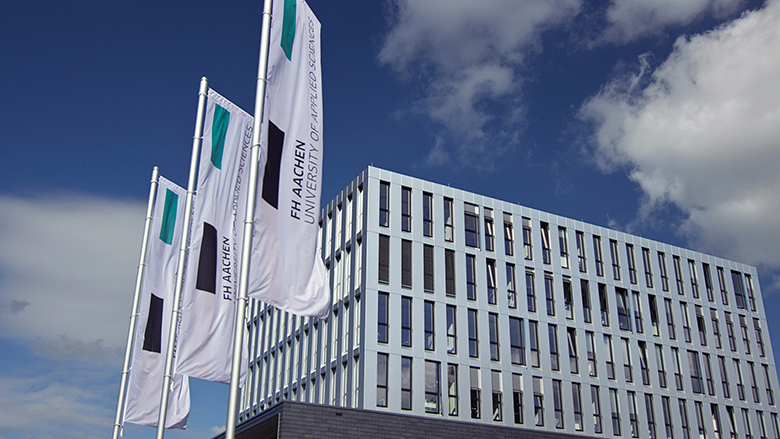 Außenansicht Fachhochschule Aachen mit wehenden Fahnen und Logo der FH auf der rechten Seite