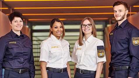 Vier Personen tragen eine Uniform, auf der "Justiz" steht und lächeln in die Kamera.