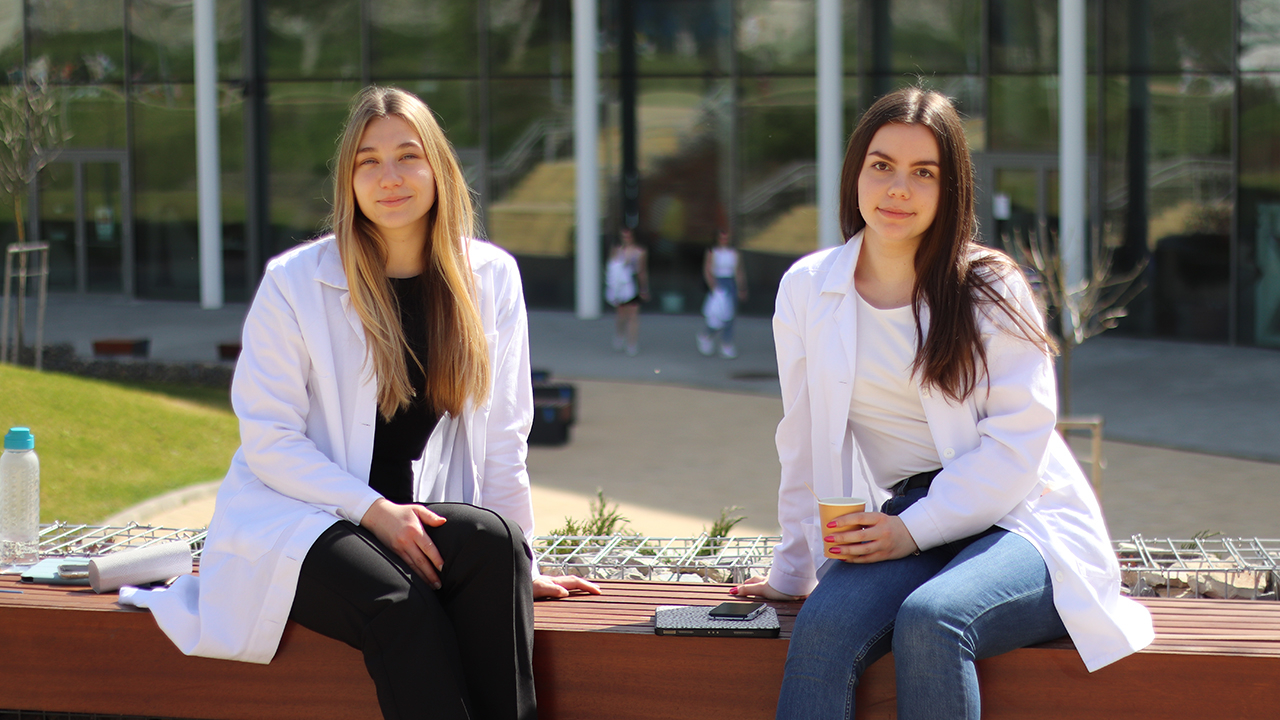 Zwei Studentinnen sitzen vor dem Unigebäude