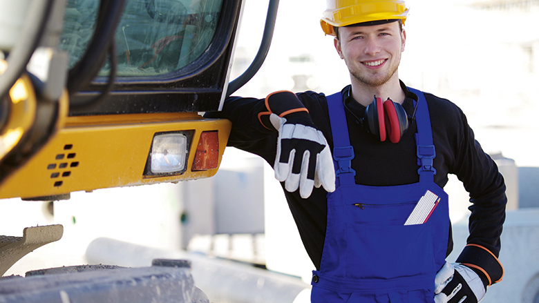 Bauarbeiter in Schutzkleidung neben Baufahrzeug