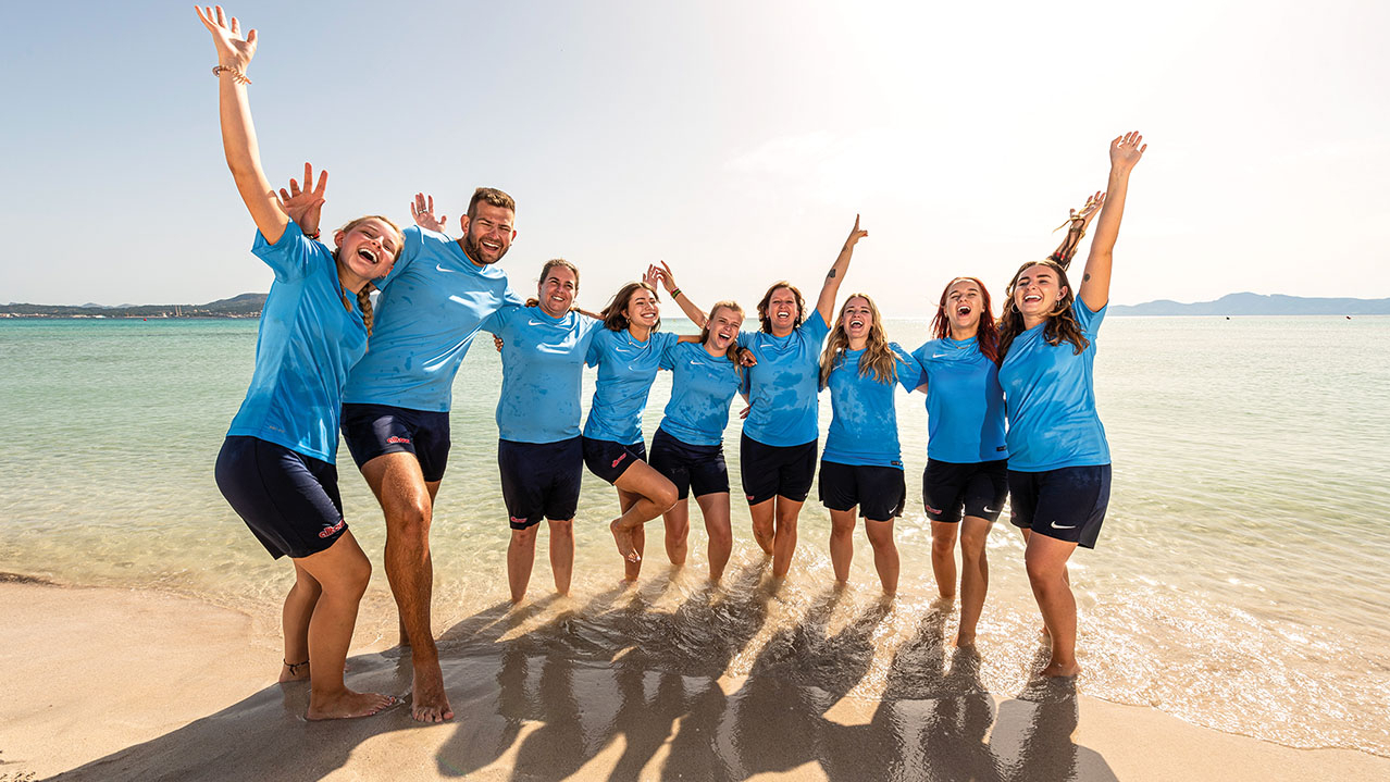 Junge Menschen in einheitlicher Clubkleidung stehen Arm in Arm im Meer