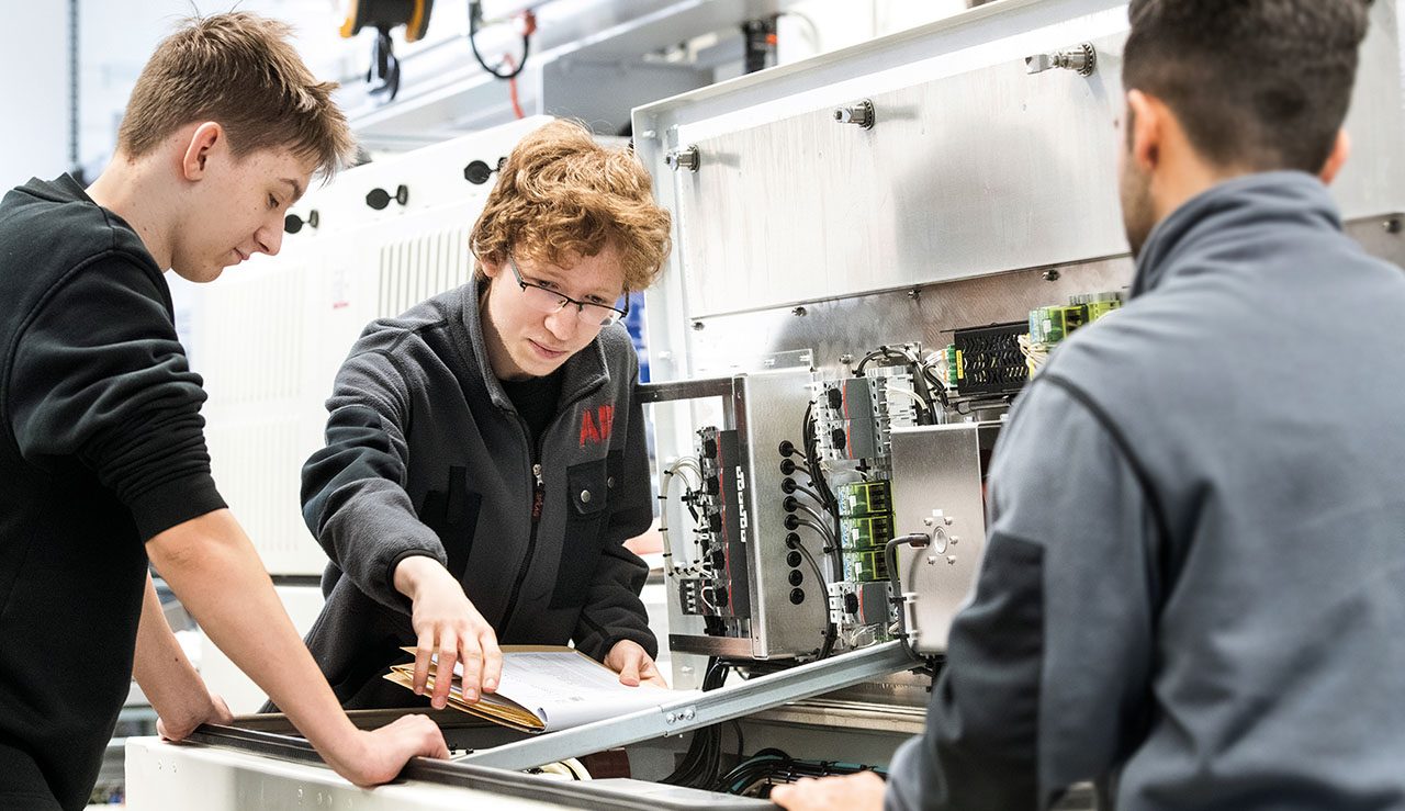 drei Jugendliche arbeiten an einer Maschine