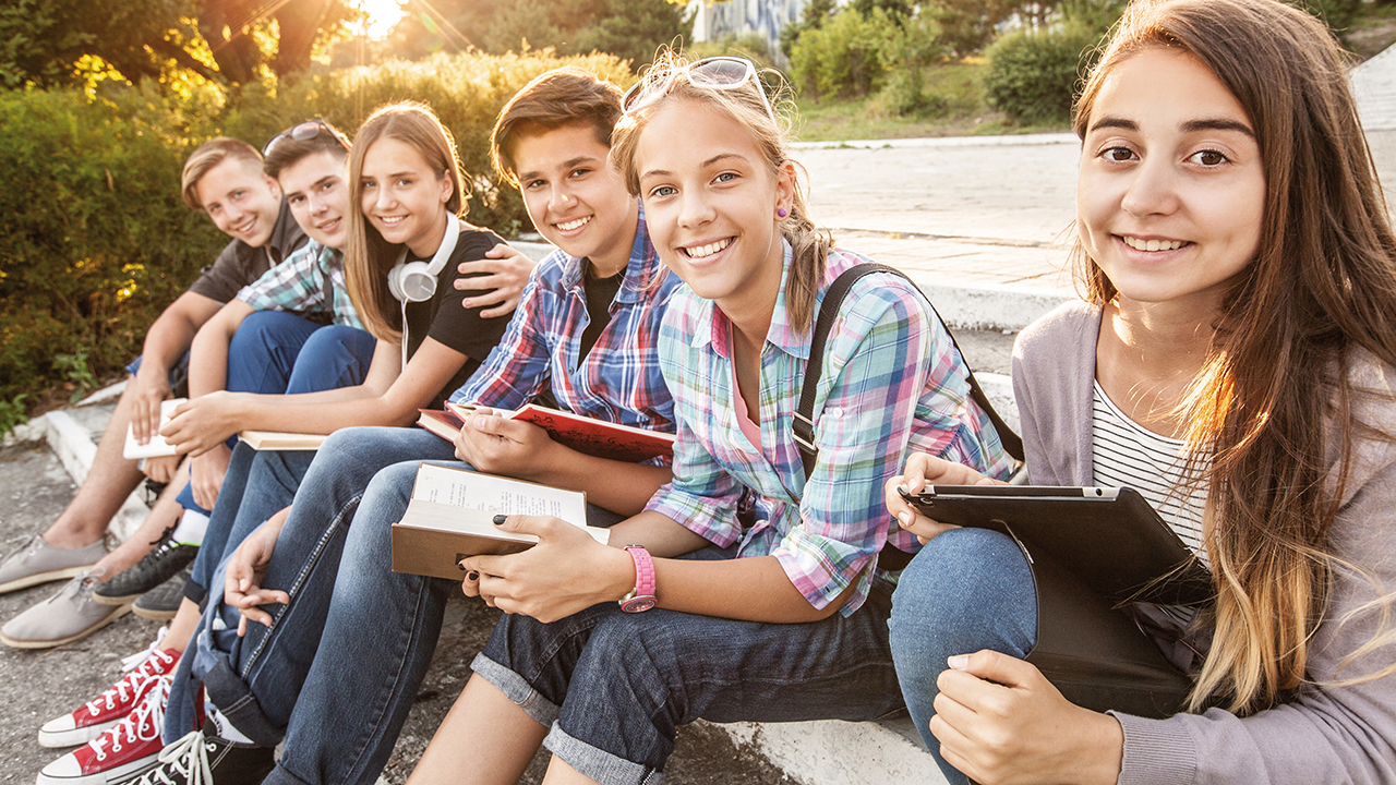 Eine Gruppe von Schülerinnen und Schülern sitzt auf einer Steintreppe in einem Park