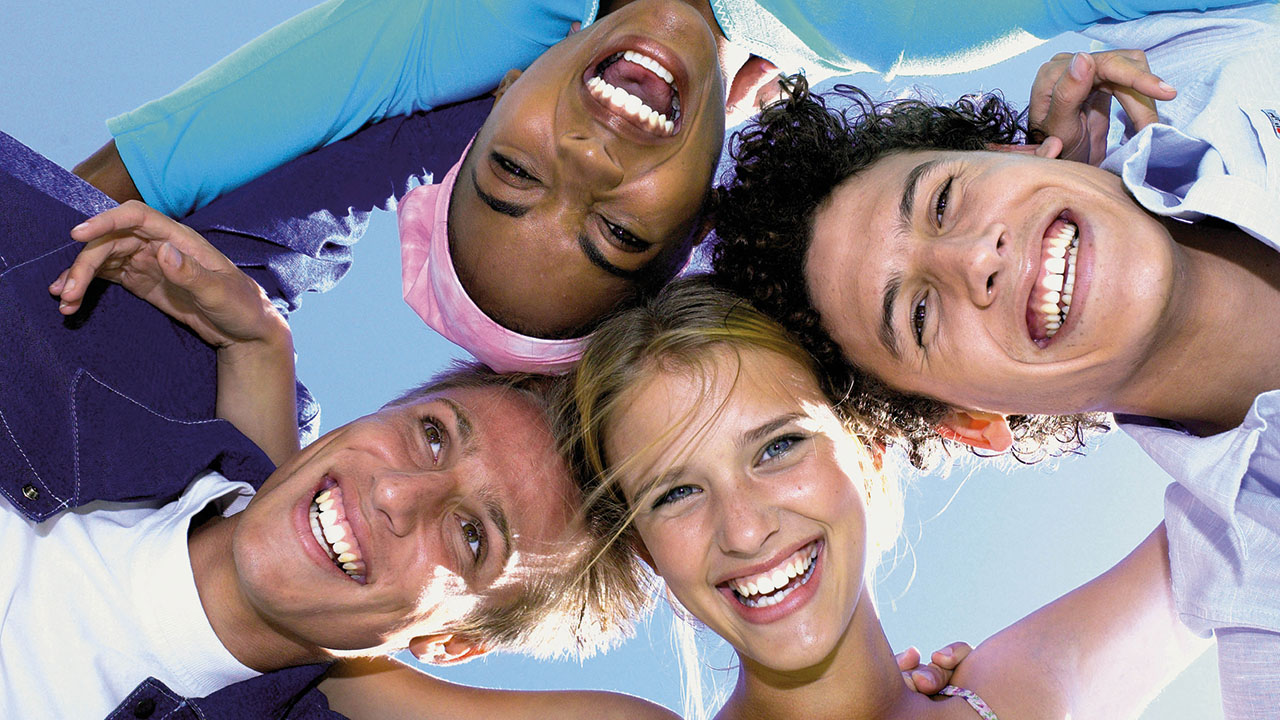 Vier junge Menschen im Kreis lächeln in die Kamera, Bild von unten aufgenommen