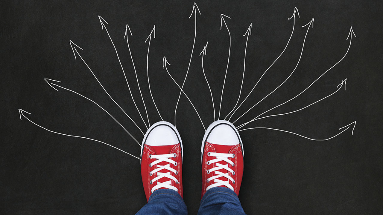 Zwei Füße in Turnschuhen, davor aufgemalte Pfeile in verschiedene Richtungen