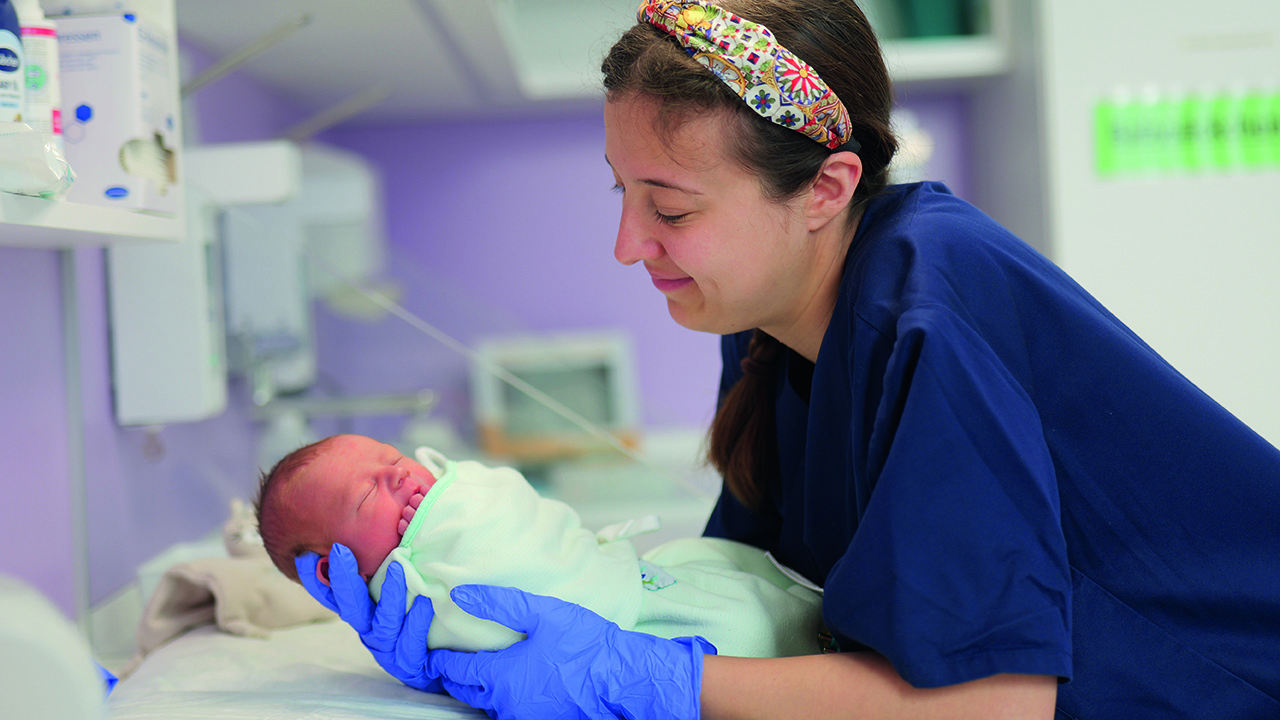 Hebamme hält frisch geborenes Baby in der Hand