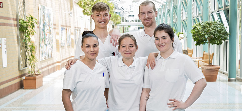Fünf lächelnde Auszubildende in Pflegebekleidung im Krankenhausflur