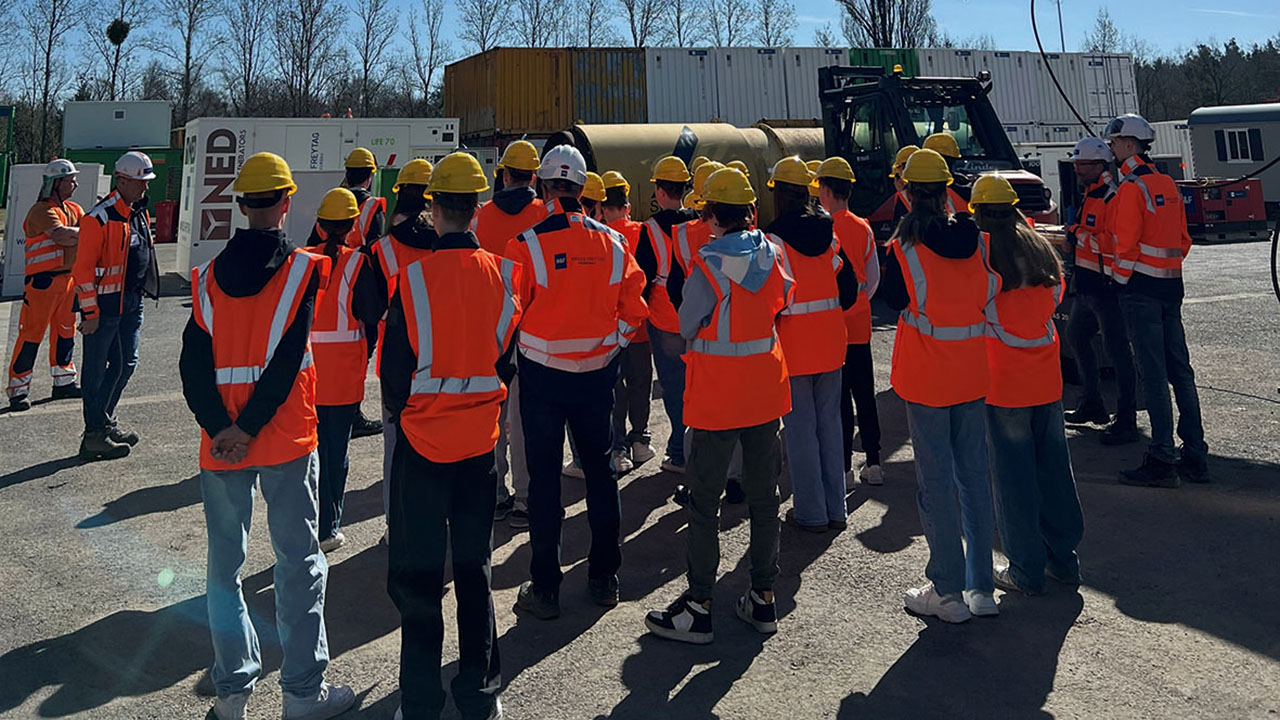 Gruppe von Menschen in orangefarbenen Westen mit Schutzhelm auf einer Baustelle