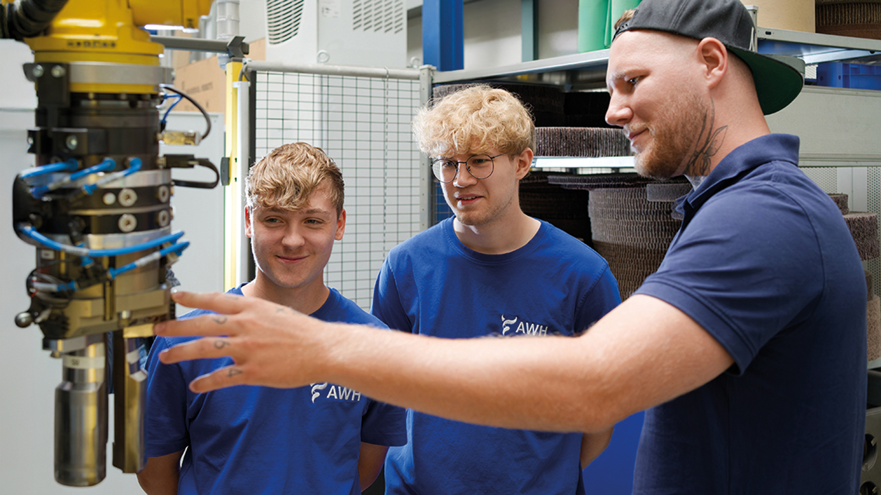 Ausbilder erklärt zwei Auszubildenden ein technisches Gerät.