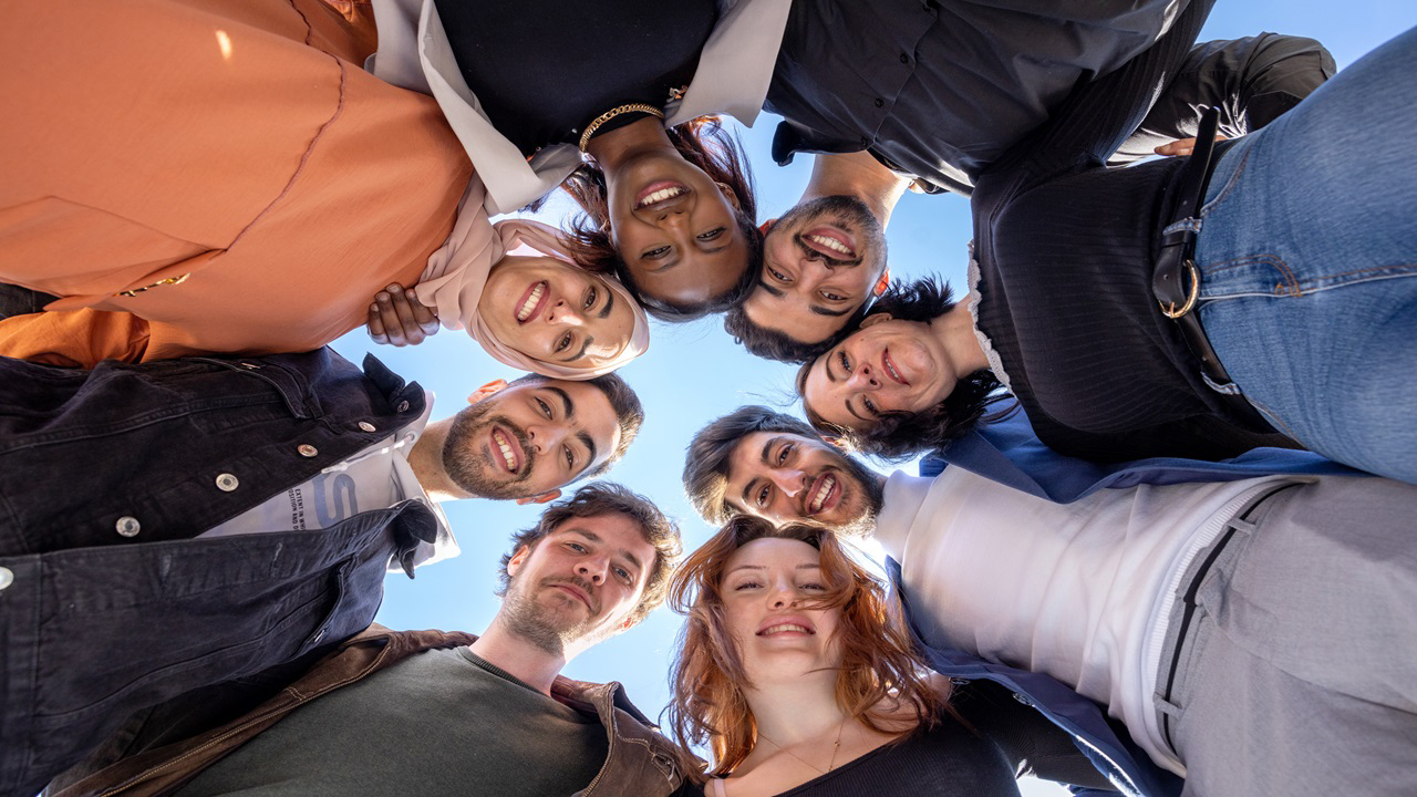 Menschen stehen im Kreis zusammen und lachen von oben in die Kamera
