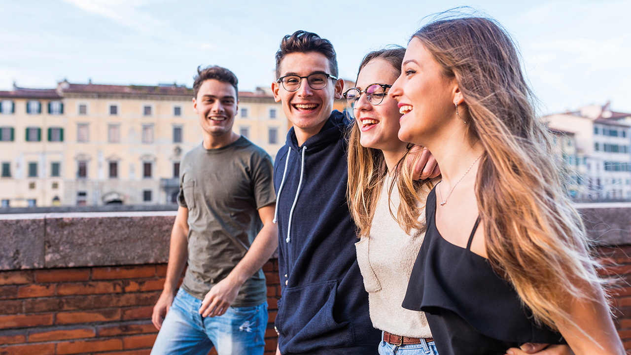 Vier junge Menschen laufen gemeinsam lächelnd an Häusern vorbei.