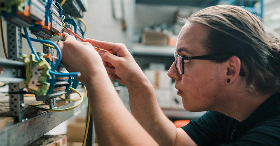 Junge Person mit Brille schraubt an einer Schaltanlage