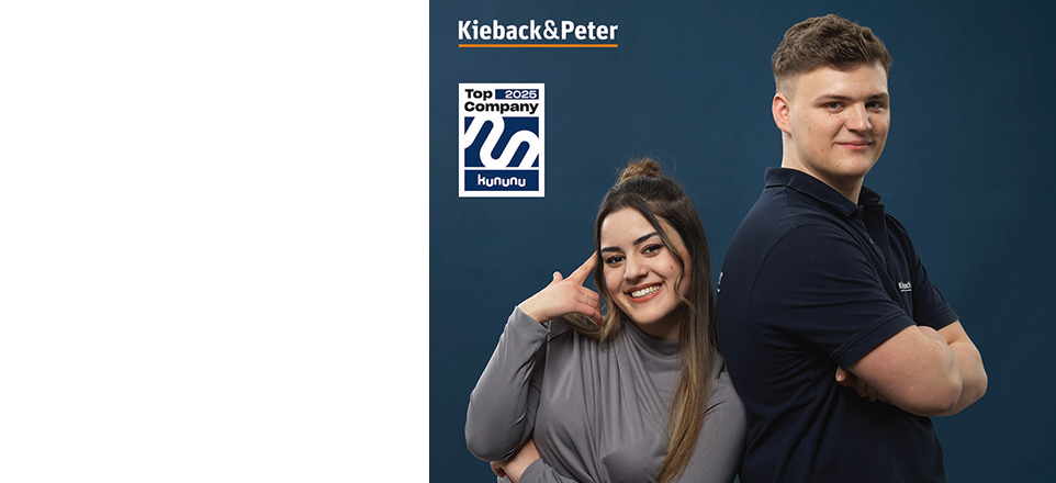 Zwei Personen lehnen sich Rücken an Rücken und lächeln in die Kamera. 