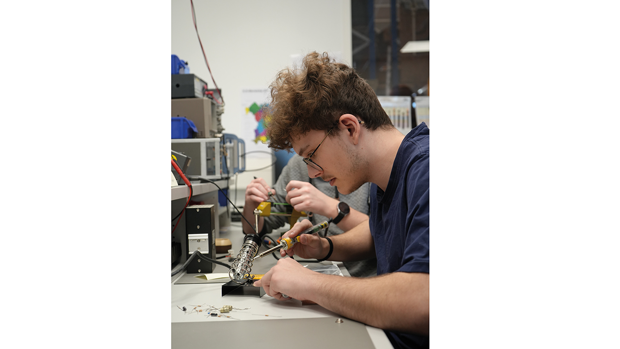 Junger Mann arbeitet mit einem Lötkolben an einem Tisch